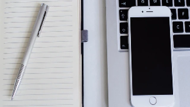 Pen and iPhone on a desk with notepad and laptop computer