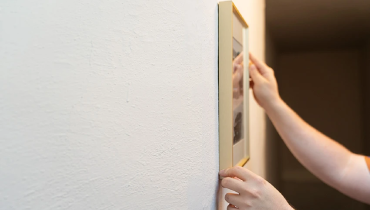 Hanging a framed picture on a white plaster wall.